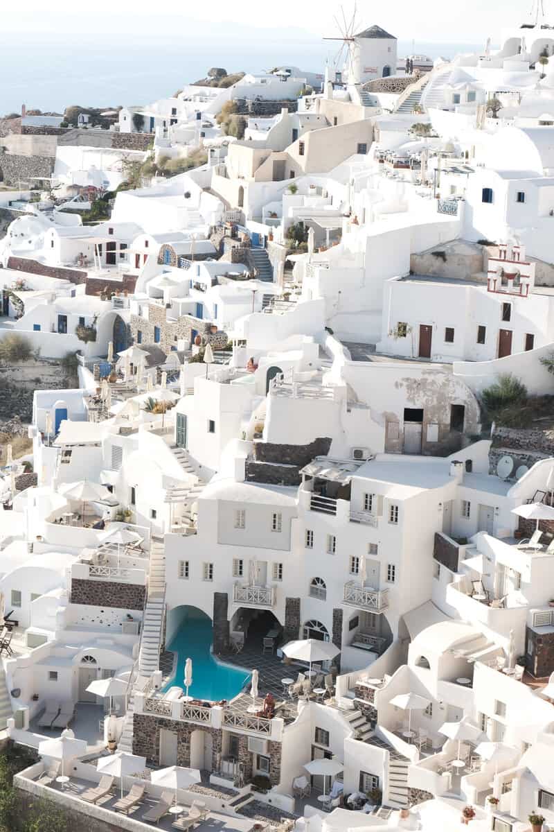 is Santorini worth visiting? white houses with swimming pools and a mill in the distance