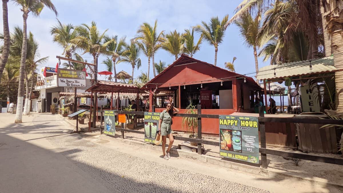 A lively beach bar with people strolling by, enjoying the vibrant atmosphere and scenic view.